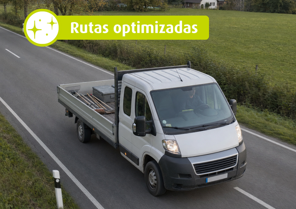 Camión blanco con plataforma abierta circulando por una carretera rural. Texto en la imagen: «Rutas optimizadas».